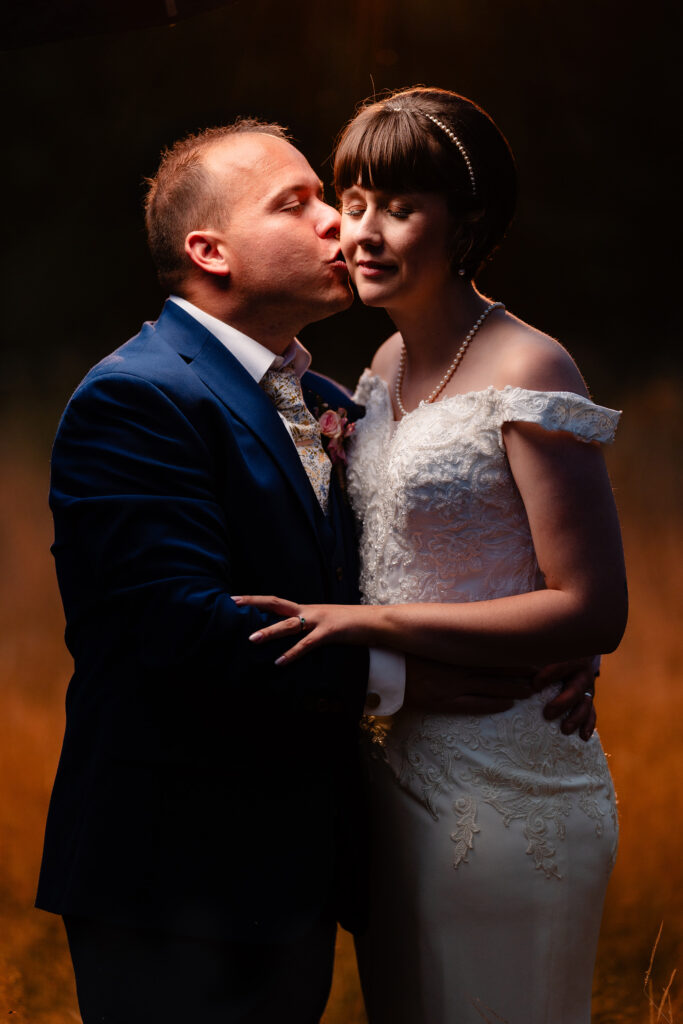 Groom kissing the bride on the cheek in warm golden light, Cheshire wedding photographer