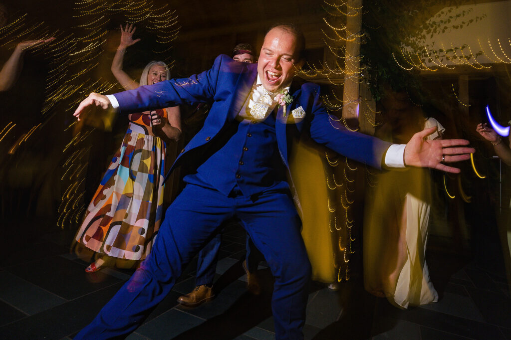 Groom throwing his arms out mid dance as guests cheer behind him