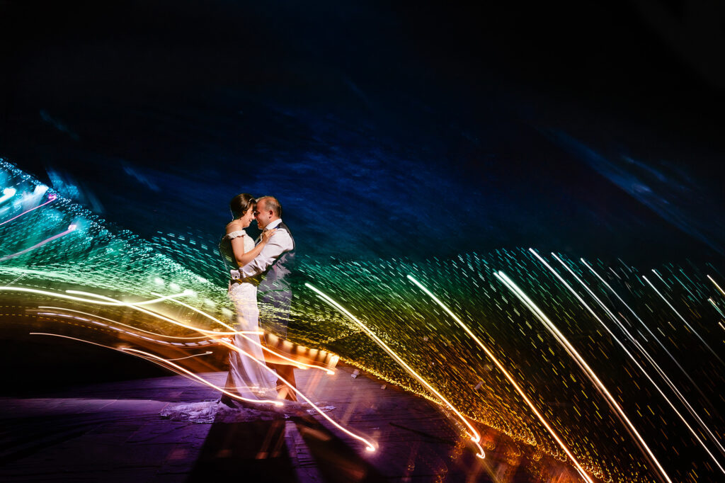 Night portrait of the bride and groom embracing as rainbow light trails sweep around them at The Oak Tree of Peover