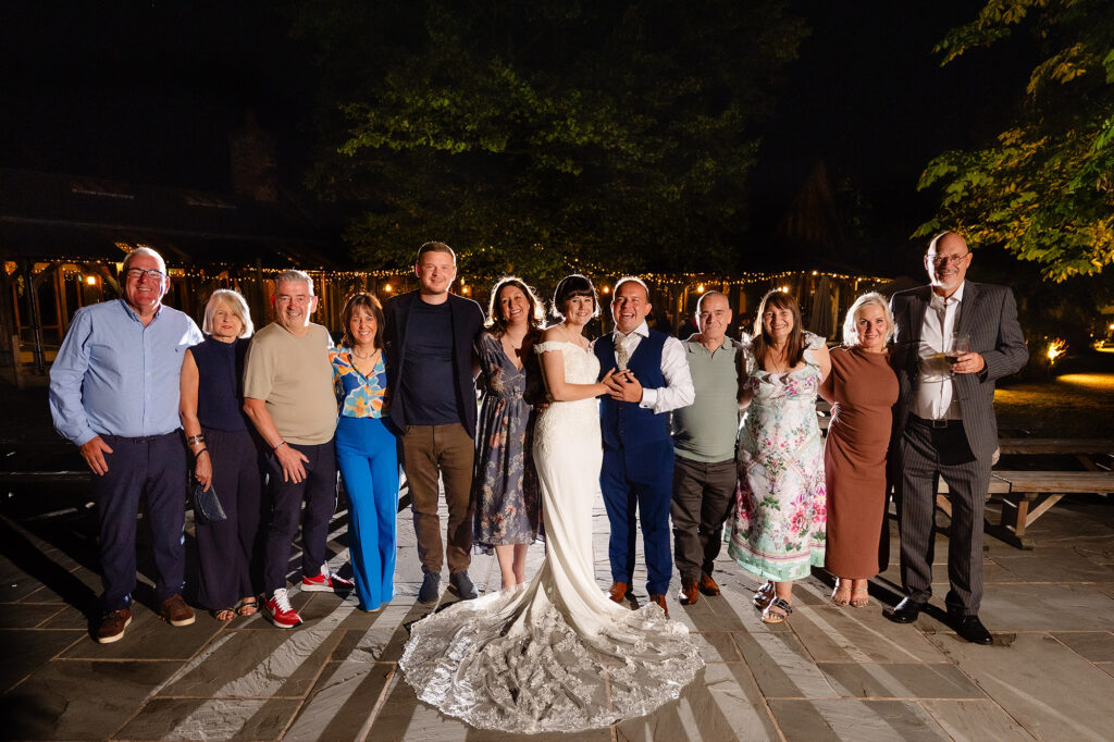Night time group photo of the newlyweds with guests outside under the festoon lights
